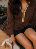 A woman wearing a brown long-sleeve blouse with gold coin trim along the V-neckline, sitting next to a tan and white dog on outdoor stone steps.